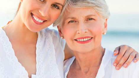 A woman and her mother smile for a picture on the beach.