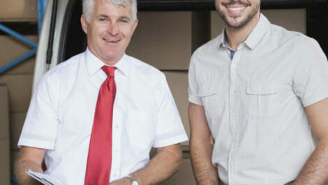 Two business partners stand in front of a car and warehouse full of boxes