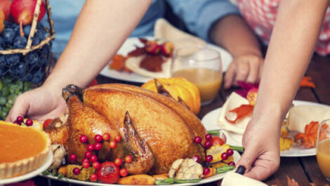 Person putting a baked turkey down on a table surrounded by people.