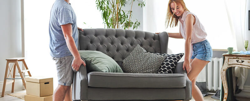 A couple works together to move a large gray chair