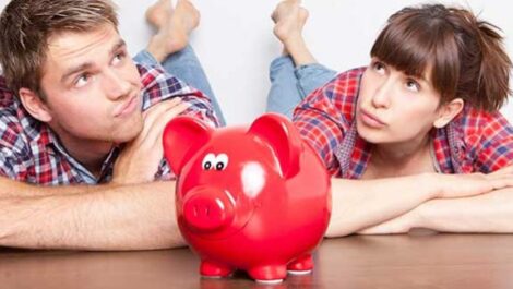 Couple sitting on the ground with a piggy bank in front of them.