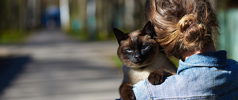 Woman holding her cat on the sidewalk.