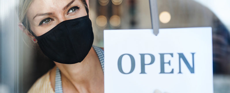 Woman with mask standing next to open sign.