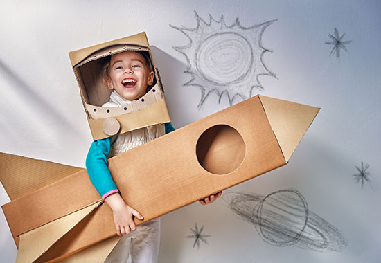 little boy posing with homemade cardboard rocket made out of moving boxes
