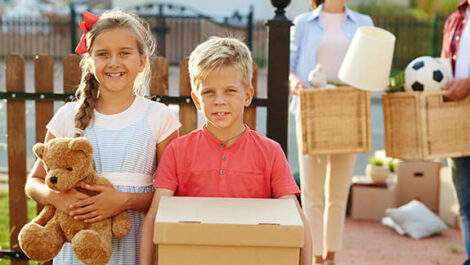 Two kids helping their parents move, holding boxes and toys.