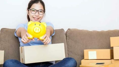 Teenager sitting on a couch, holding out a yellow piggy bank.