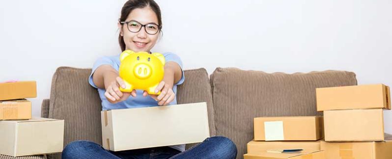 Teenager sitting on a couch, holding out a yellow piggy bank.