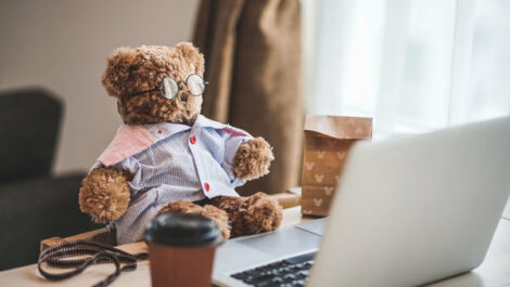 A stuffed teddy bear sits in front of a laptop
