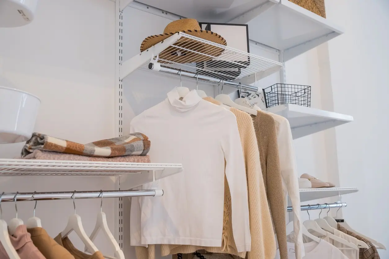 brightly lit closet filled with sweaters, hats, and scarves hanging on a wire closet organizational system