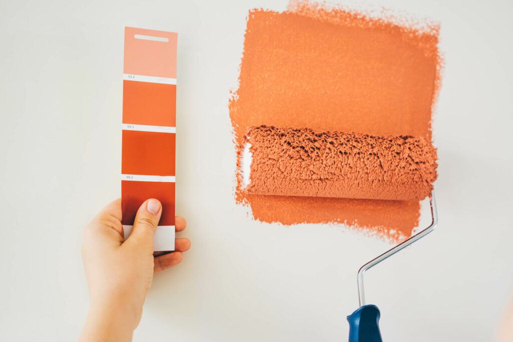Unseen person swatching burnt orange paint next to paper swatch.