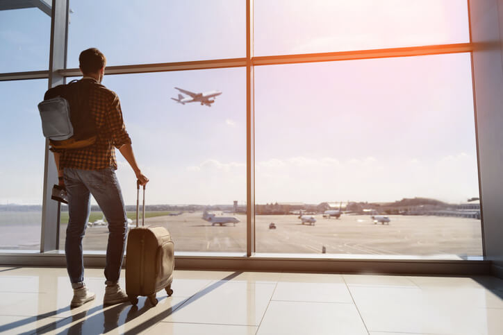 Man standing at airport window watching planes take off. 