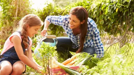 Mother wattering garden while daughter pots plants.