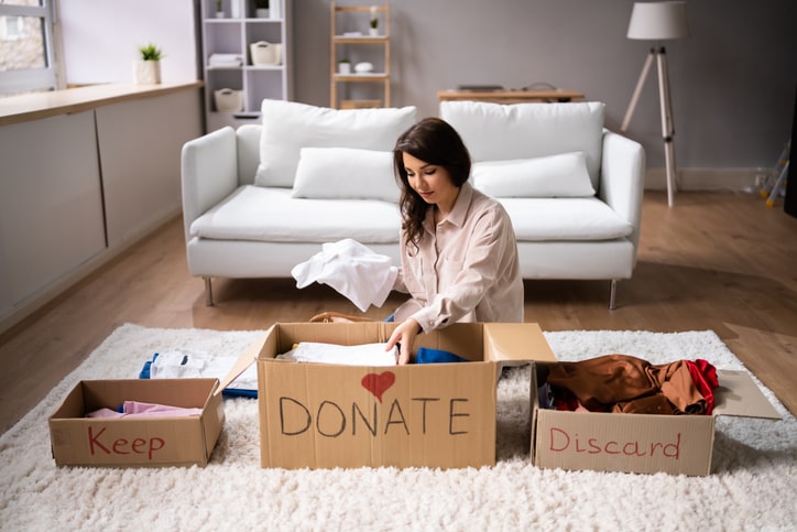 A woman sits on the floor sorting belongings into labeled boxes.