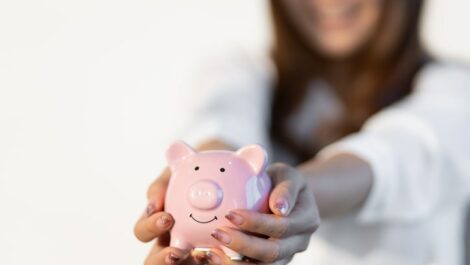 Woman with glitter manicure holding a pink piggy bank