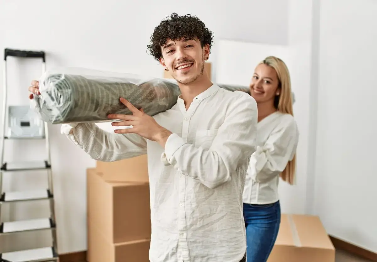 A young,smiling couple carrying a rug while moving