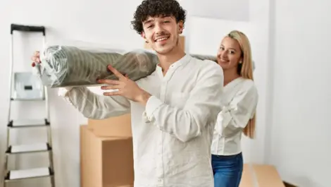 A young,smiling couple carrying a rug while moving