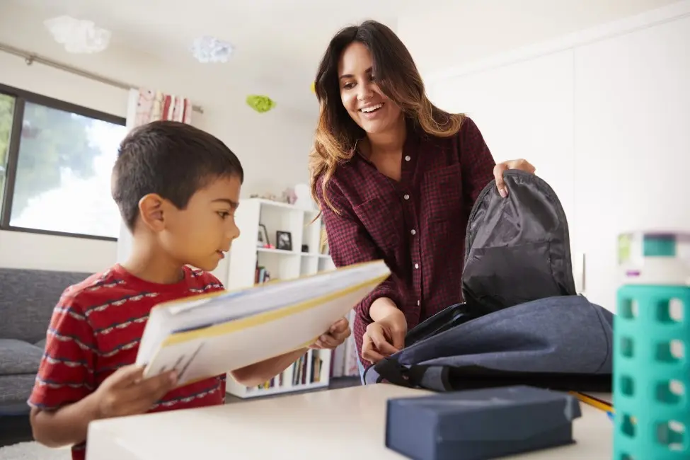 Mother smiles and helps young son pack up school bag