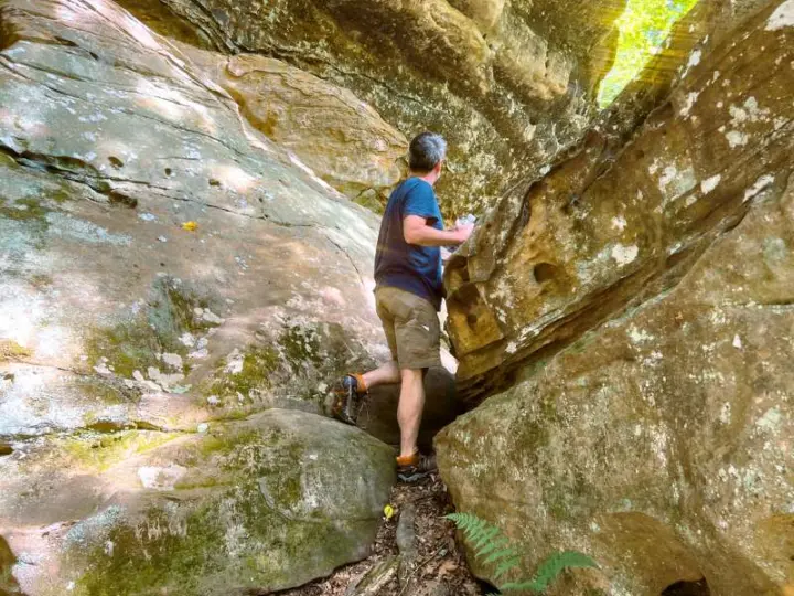 A man in hiking gear squeezes between two large, moss-covered rocks