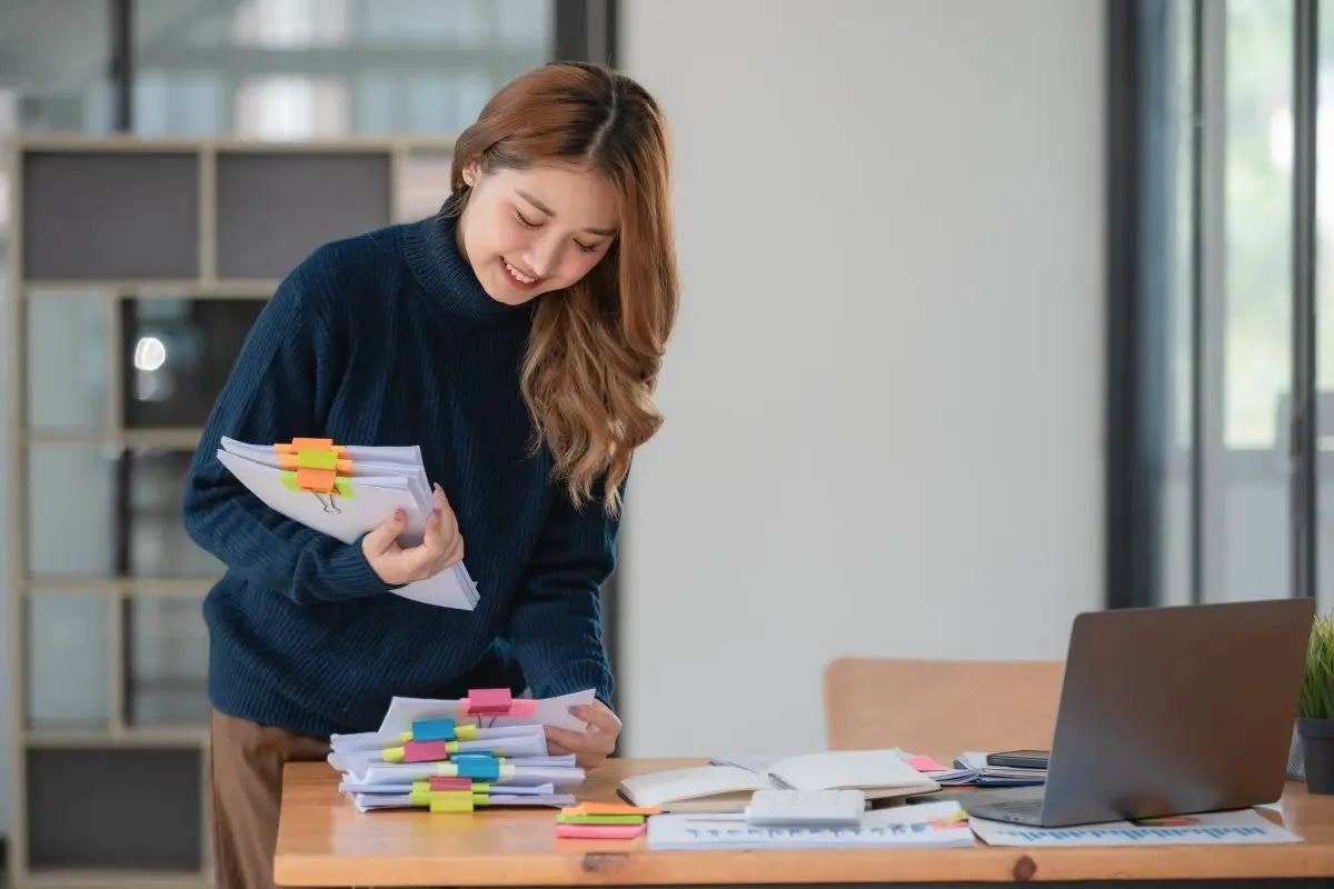 Teacher smiles while grabbing organized papers with colorful clips 