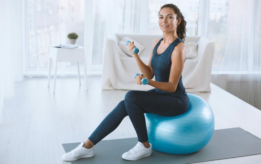 Woman lifts dumbbells while sitting on a yoga ball during a home workout