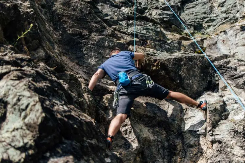 A man wearing a blue shirt climbing up a steep rock face, clipped onto a rope