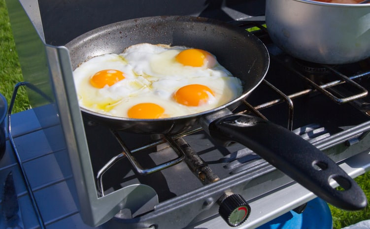 Fried eggs simmering on a skillet over a camp stove