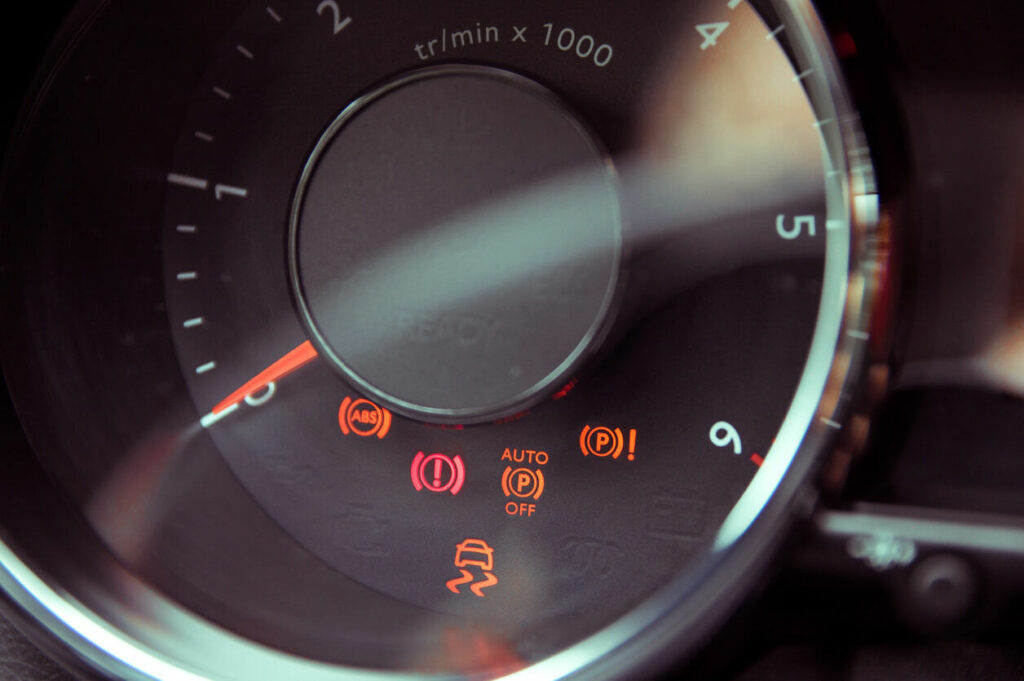 A car dashboard with traction control, parking brake, and ABS lights illuminated