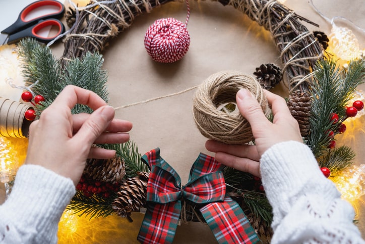 A person crafts a holiday wreath using twine