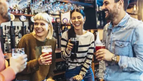 Smiling and laughing young friends drinking craft beer in a pub.