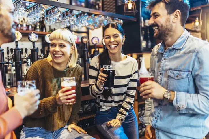 Smiling and laughing young friends drinking craft beer in a pub.