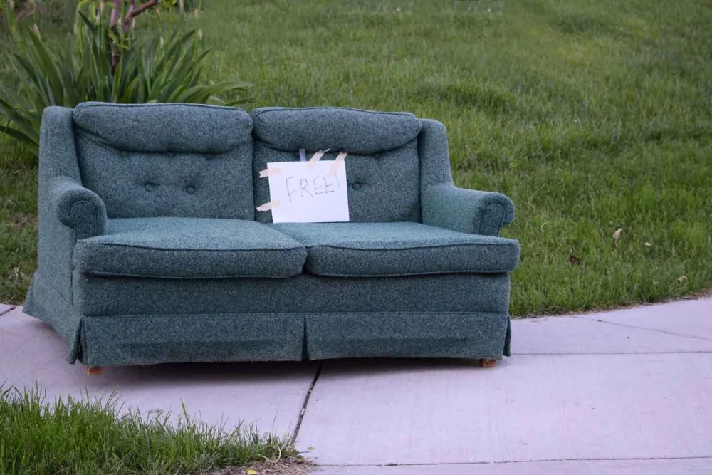 A couch sitting on the sidewalk with a sign that says “free”