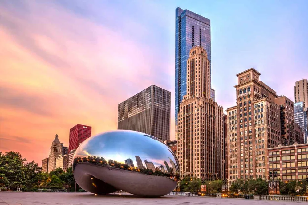 A photograph of the Bean in Chicago, with skyscrapers and a sunset behind it