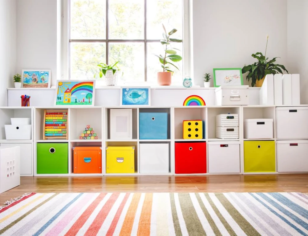 A white cubby system holds rainbow bins and toys in a grade school classroom