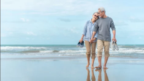 Elderly couple holding hands while walking on the beach.