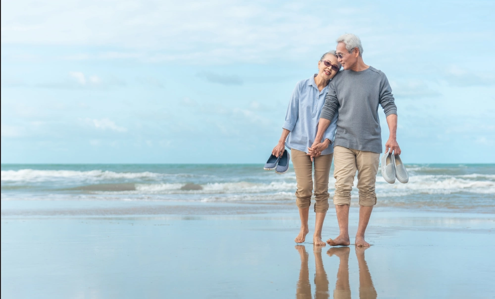 Elderly couple holding hands while walking on the beach.