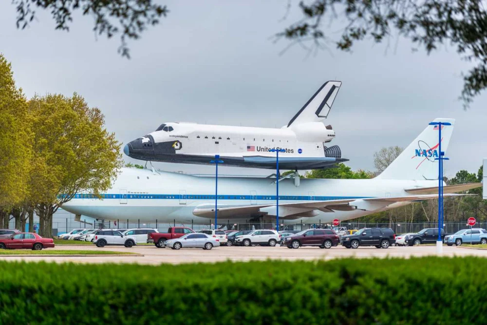 An Image of a space shuttle sitting on top of another aircraft at the Johnson Space Center in Houston, TX