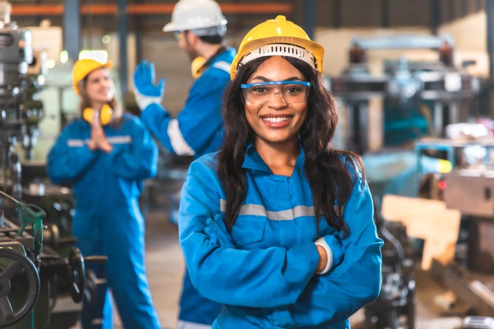 A Smiling woman faces the camera with her arms folded, wearing PPE