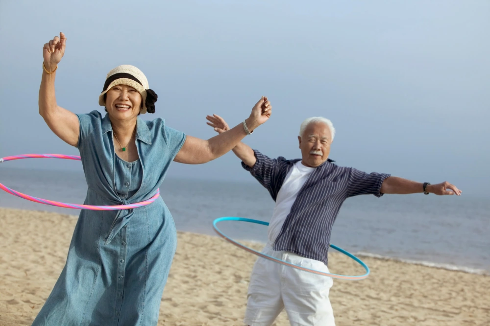 Mature couple hula-hooping on the beach.