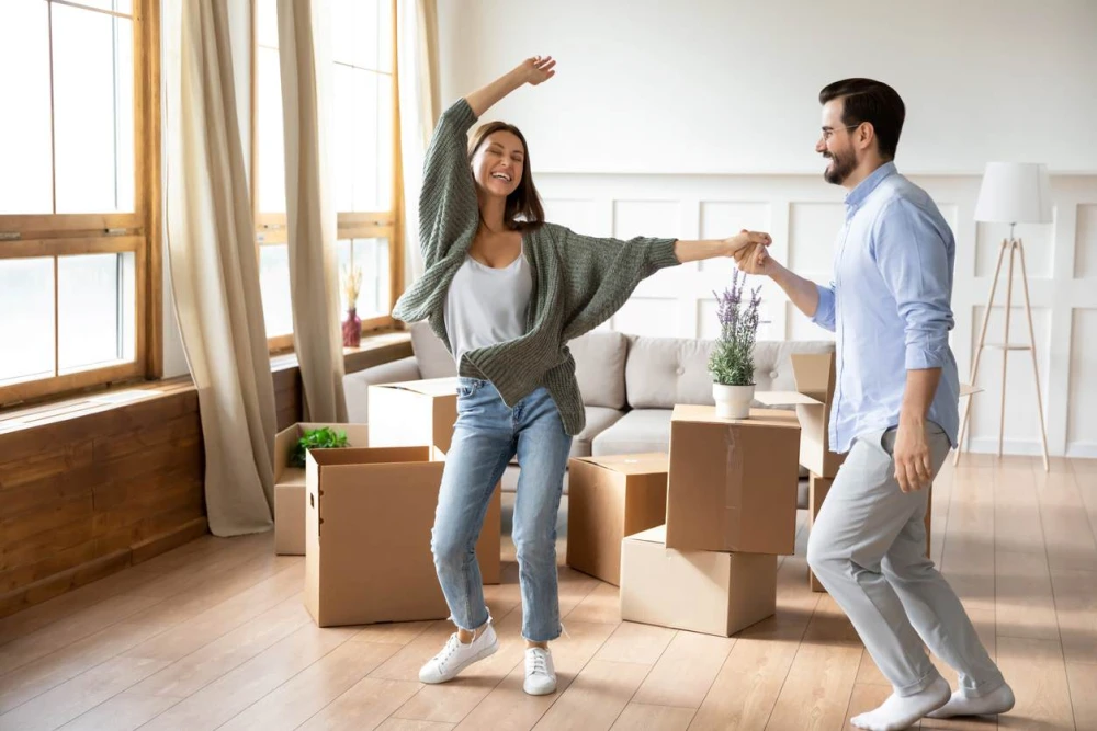 A young couple dancing in their living room, surrounded by boxes