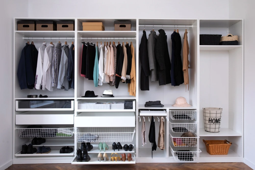 a well-organized white closet system with hanging clothes, shoes, hats, and baskets