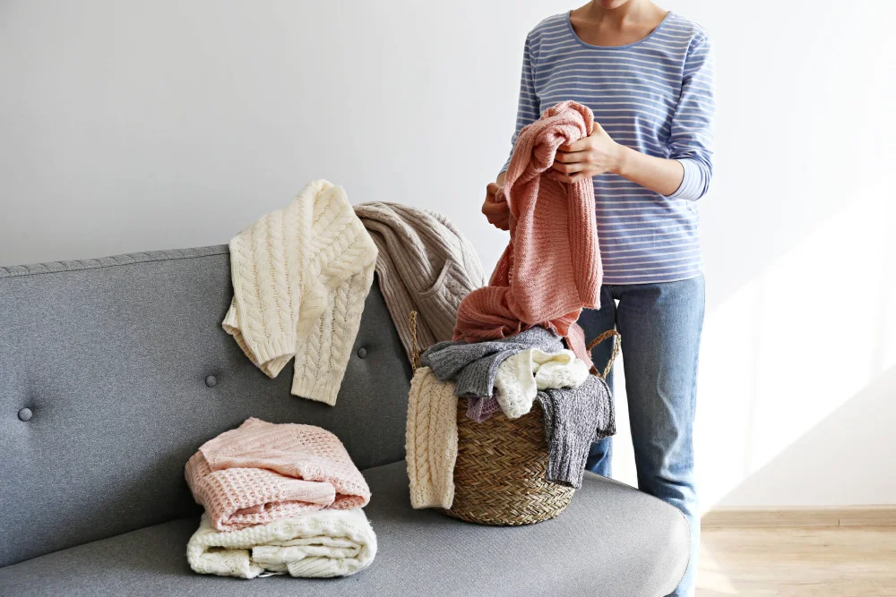Woman folding sweaters on the couch.