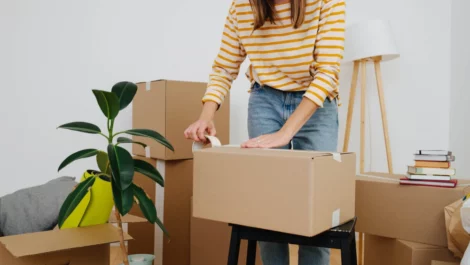 Woman taping a cardboard moving box closed.