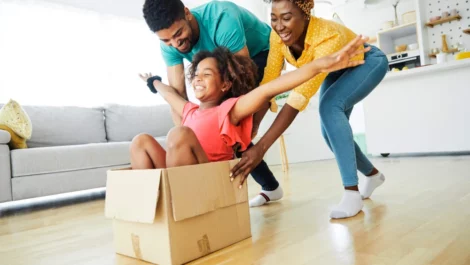Child laughing in box while parents push her across the floor.