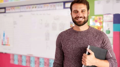 Smiling male teacher standing in front of his whiteboard