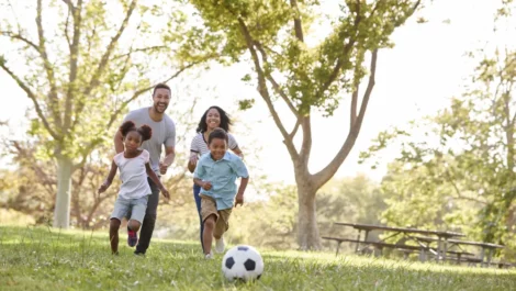 Black family playing soccer in the park together