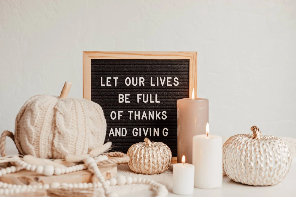 A letterboard sign reads "Let our lives be full of thanks and giving," surrounded by knitted pumpkins and candles.