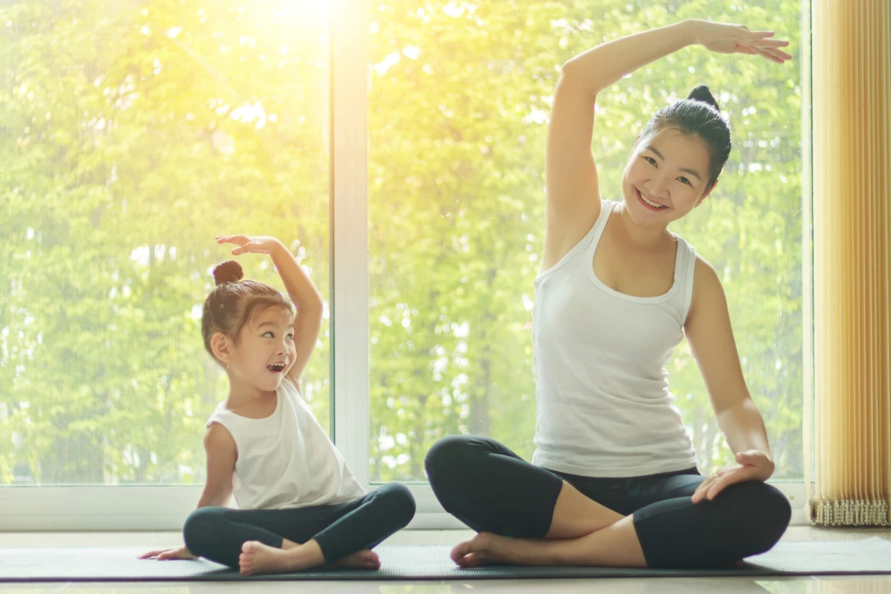 Mother doing yoga while daughter smiles and imitates her pose.