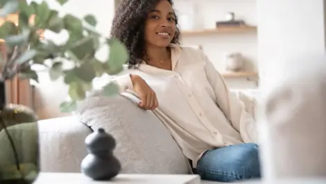 Portrait of lovely young mixed race woman smiling and looking at camera, sitting on sofa at home stock photo