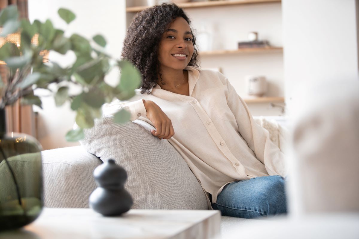 Portrait of lovely young mixed race woman smiling and looking at camera, sitting on sofa at home stock photo