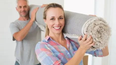 Happy couple carrying a rolled up rug together